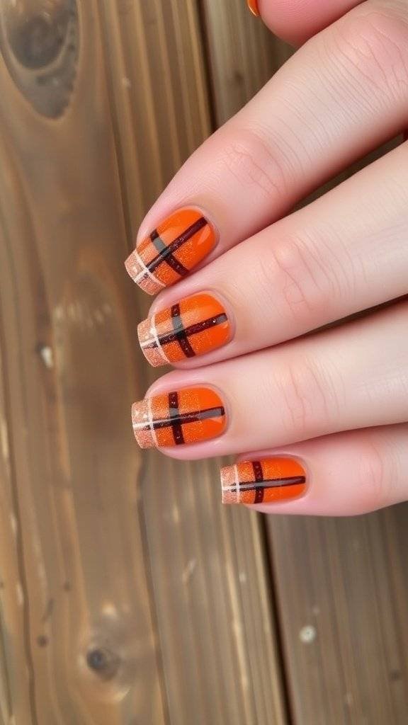 Nail art featuring rust orange plaid pattern with glitter tips on a wooden surface.